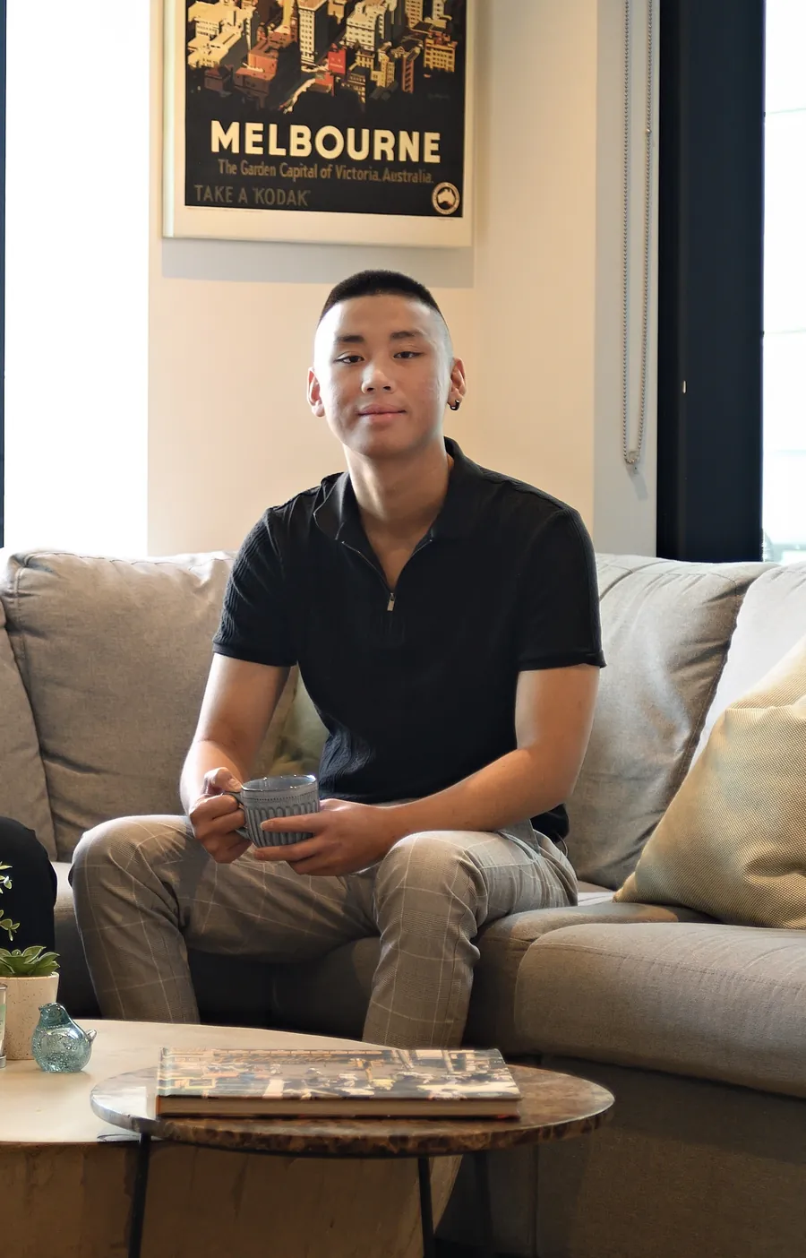 Jordan Pham on a sofa with a coffee under a vintage Melbourne poster